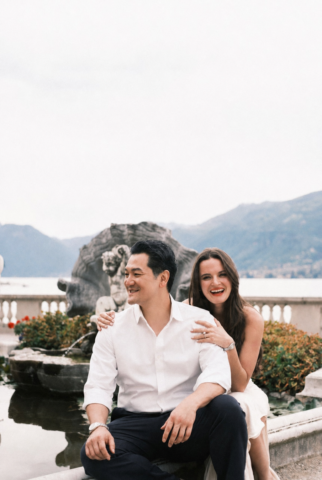 Maria & Scott smiling together beside a lakeside fountain